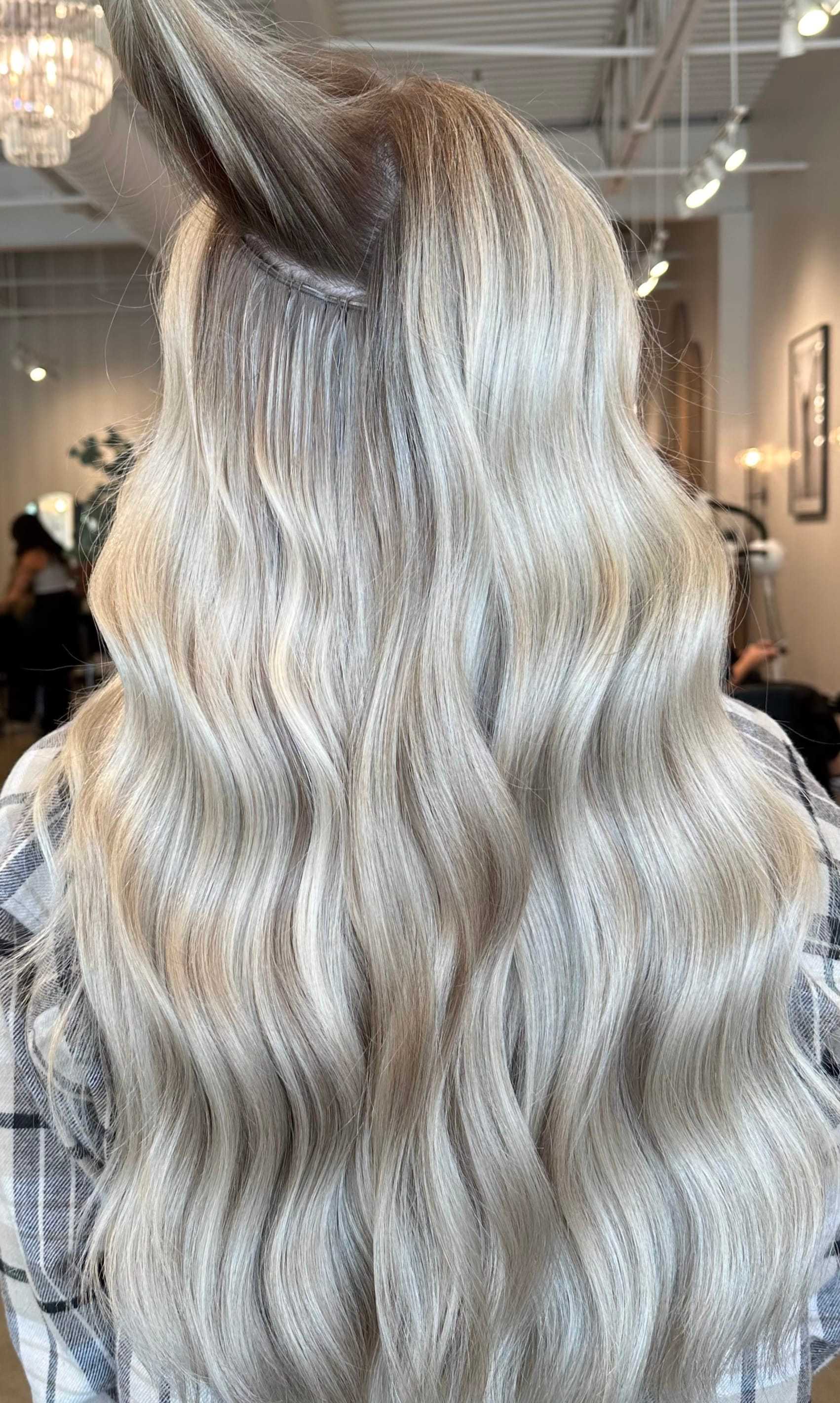 Long wavy platinum blonde hair with subtle highlights in a salon setting.